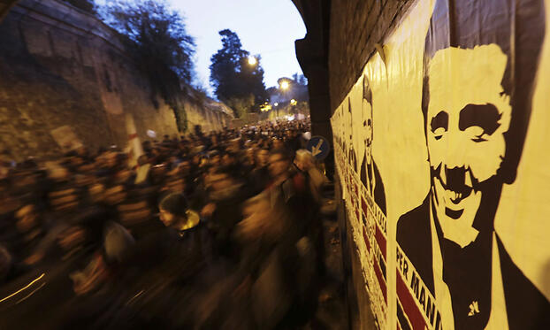 Протестующие проходят мимо плаката, изображающие Ренци во время демонстрации в Риме в преддверии референдума.
